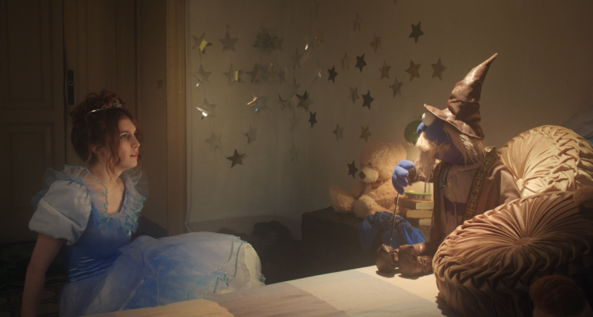 Young performer in a blue dress facing a costumed figure in a star-lit room.
