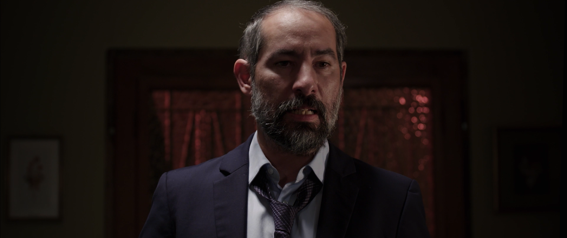 Bearded man framed in a dark motel room interior.